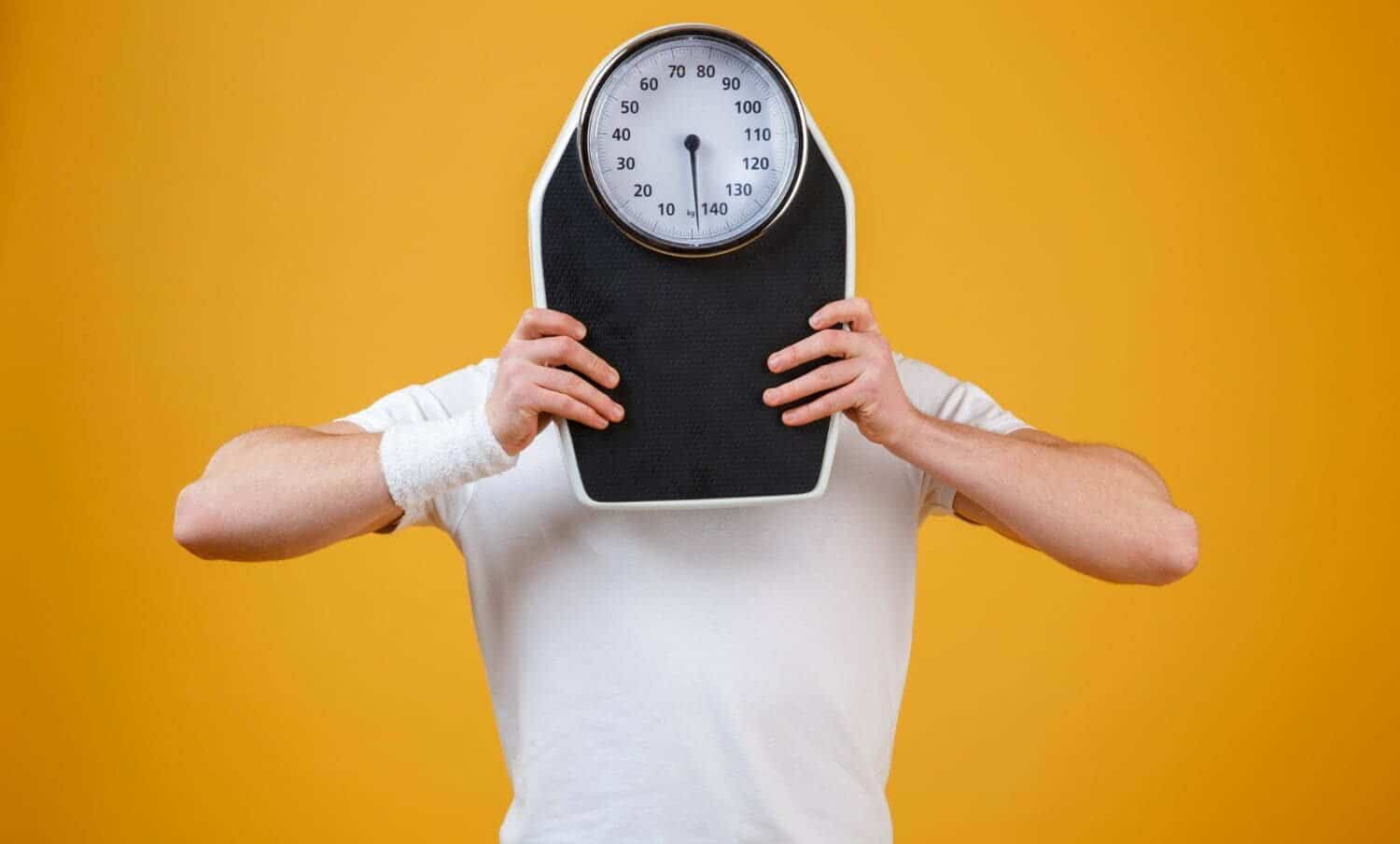 Joven deportista ocultando la cara detr&aacute;s de las escalas de peso / acelerar el metabolismo