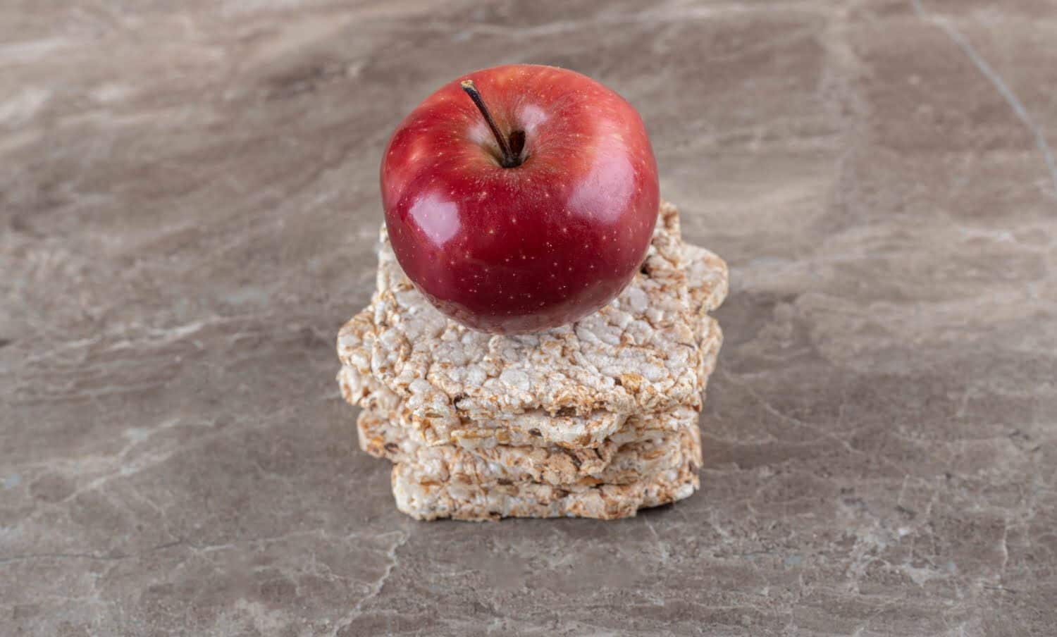 Manzana sobre pila de tortas de arroz inflado en la superficie de m&aacute;rmol