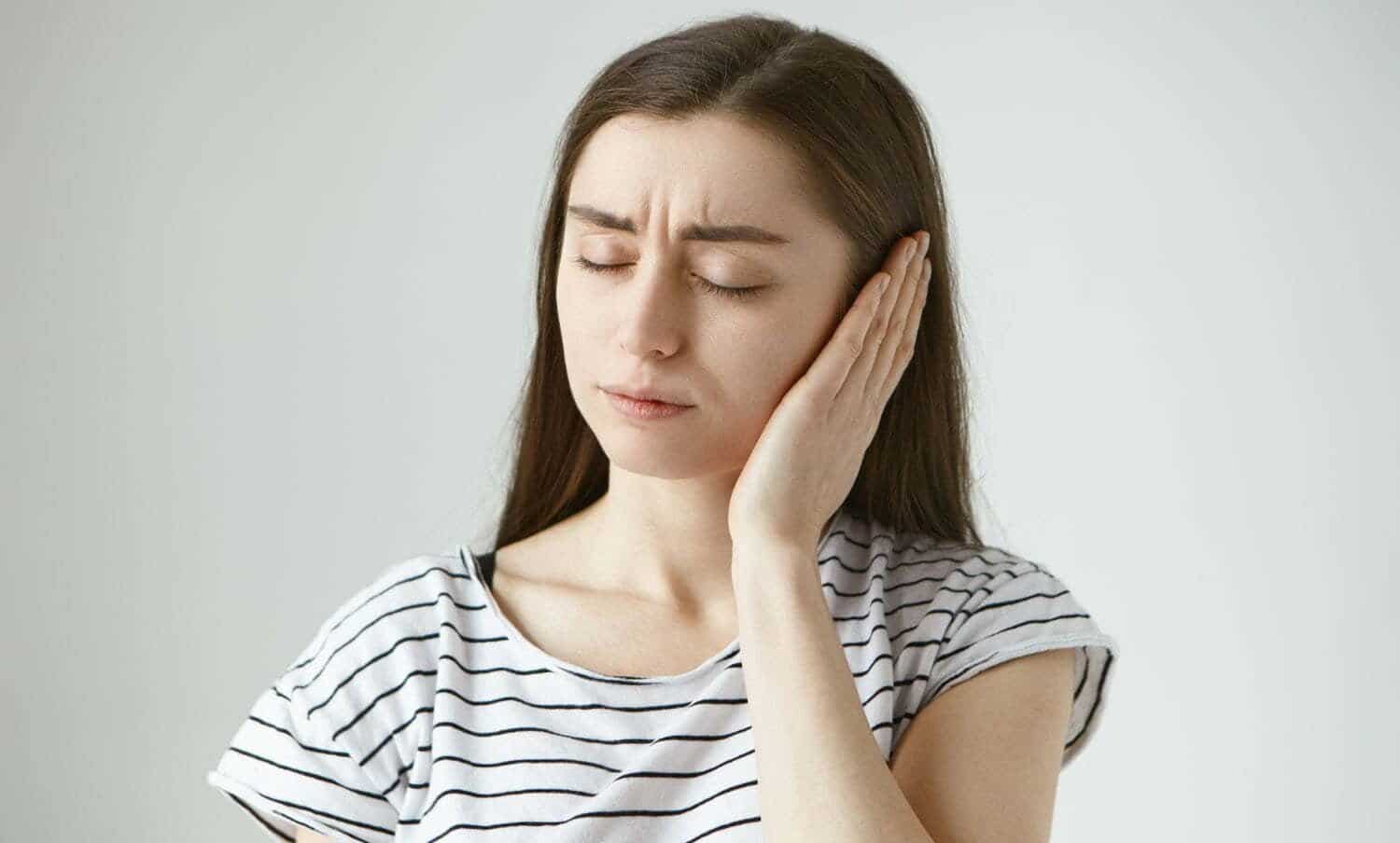 mujer joven toc&aacute;ndose el oido con cara de dolor