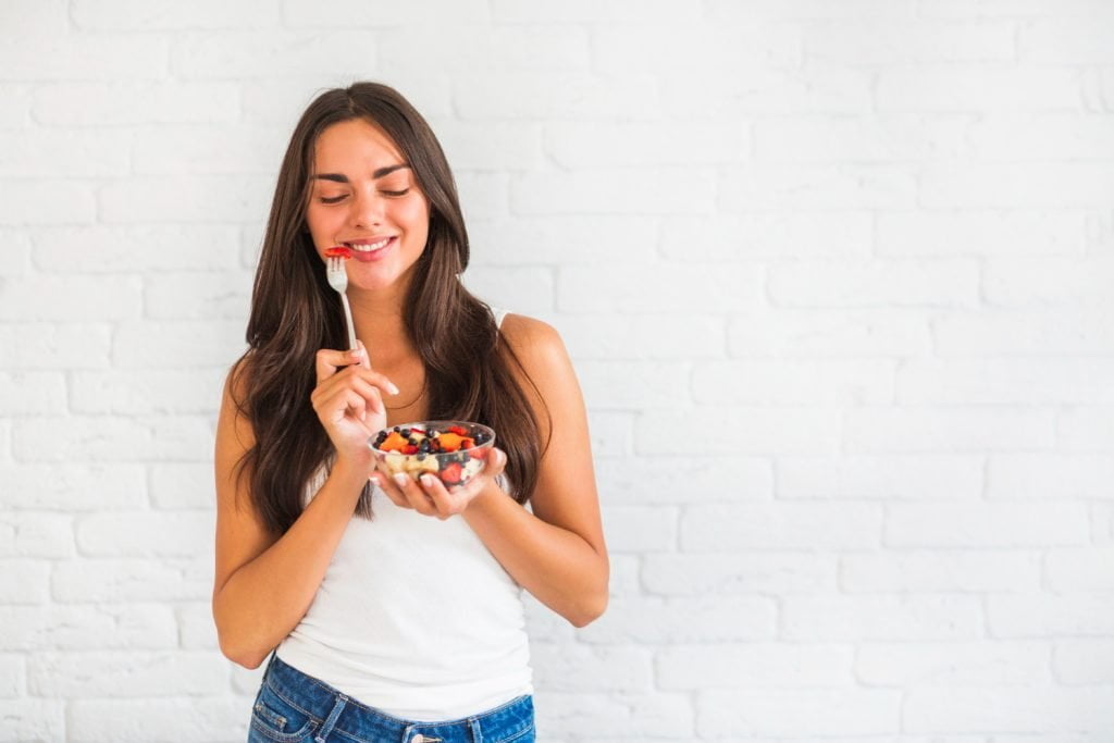 Mujer feliz comiendo una taza de frutas, sin fatiga ni cansancio / embarazo