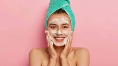 mujer sonriente con toalla en la cabeza y jab&oacute;n en la cara, con las manos en sus mejillas - lavarte la cara en la ducha