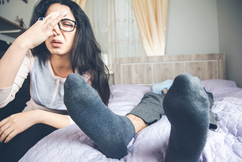 Mujer visiblemente molesta por el mal olor de los pies de su pareja / mal olor en los pies / malos olores corporales