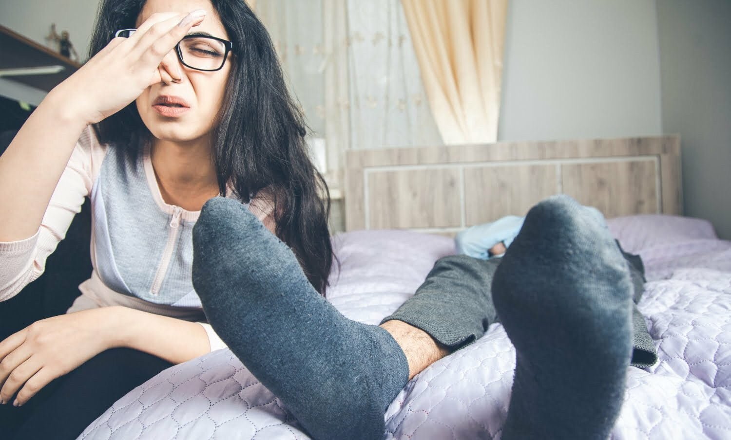 Mujer visiblemente molesta por el mal olor de los pies de su pareja / mal olor en los pies / malos olores corporales