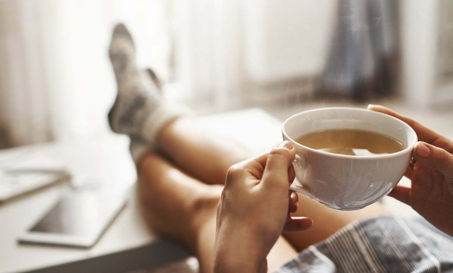 mujer acostada en el sofá, con las piernas sobre la mesa, tomando café caliente / bebidas