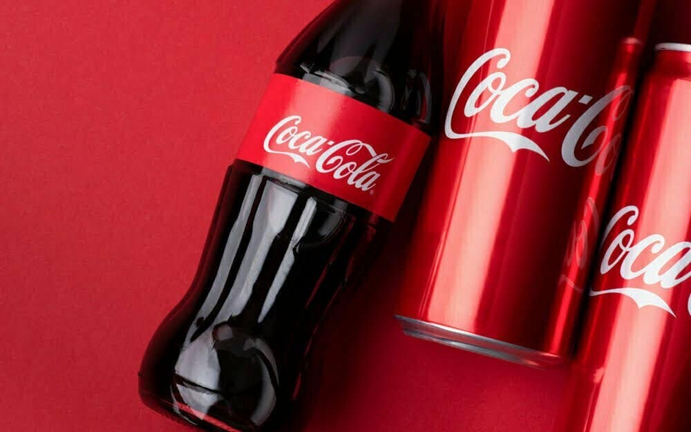 Una botella y dos latas de Coca Cola sobre un fondo rojo | Coca-Cola pirata