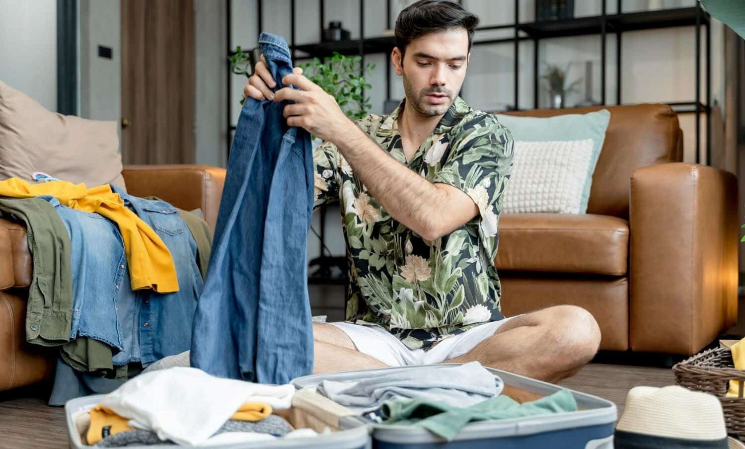 El marido cauc&aacute;sico ocupado trata de organizar la ropa de viaje / empacar tu maleta y tener m&aacute;s espacio