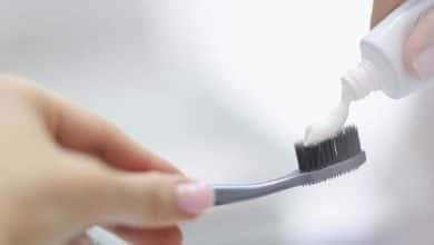 Manos femeninas apretando la pasta de dientes en el cepillo en el ba&ntilde;o / pasta dental