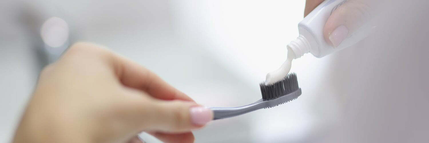 Manos femeninas apretando la pasta de dientes en el cepillo en el baño