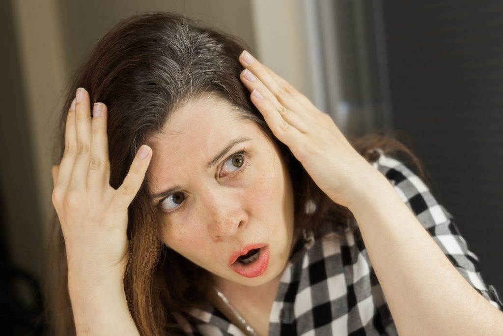 Mujer con cara de sorpresa por encontrarse canas en su cabello