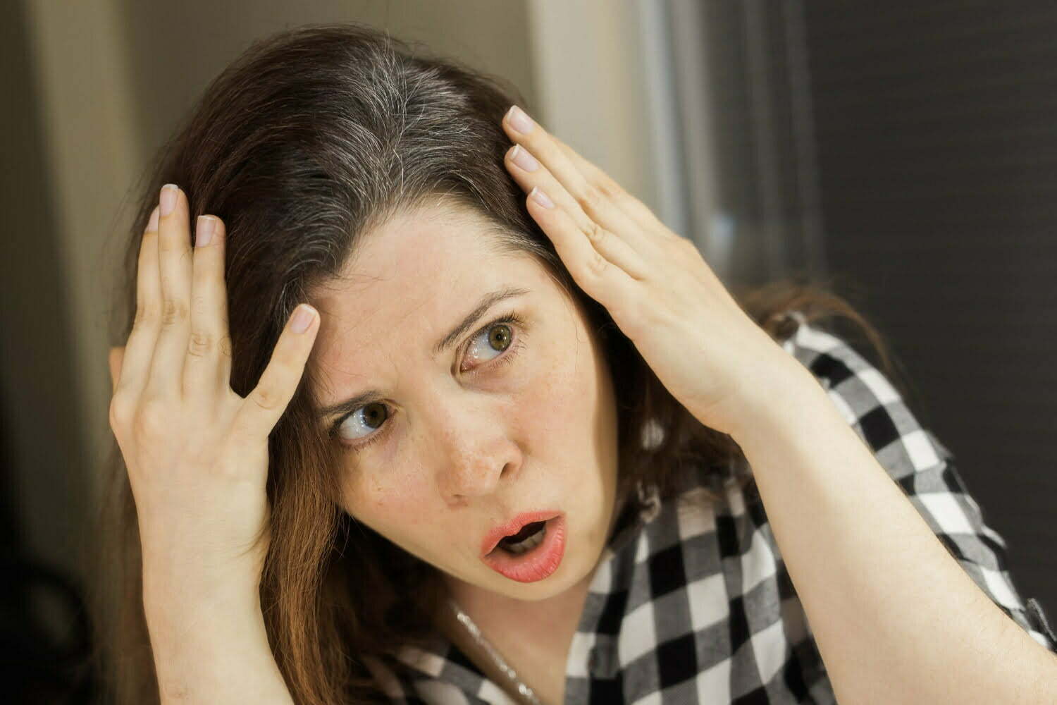 Mujer con cara de sorpresa por encontrarse canas en su cabello