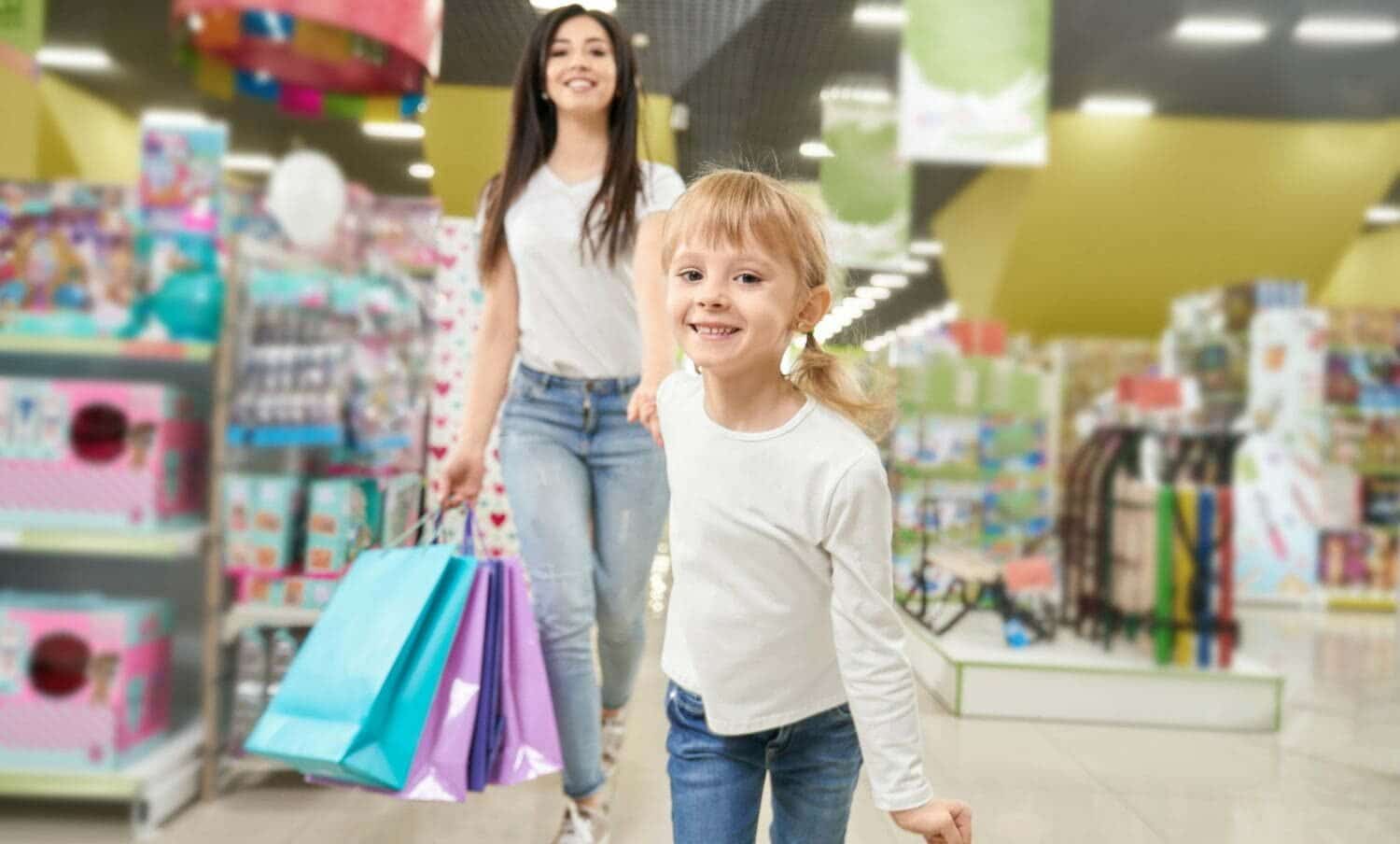 Chica manteniendo la mano de mam&aacute; y corriendo hacia adelante en jugueter&iacute;a / juguetes