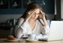 mujer en escritorio frente a su computador, sufriendo de dolores de cabeza | aliviar el dolor de cabeza / sed / dolores de cabeza