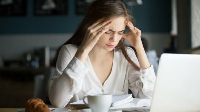 mujer en escritorio frente a su computador, sufriendo de dolores de cabeza | aliviar el dolor de cabeza / sed / dolores de cabeza