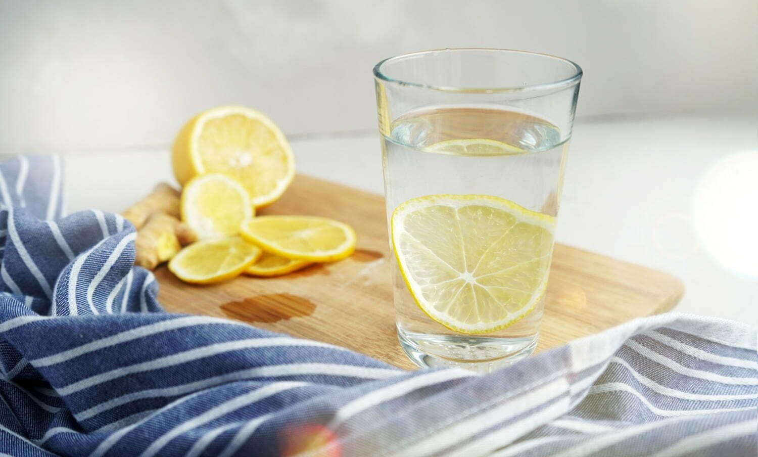 vaso de agua tibia con una rodaja de limón junto a una servilleta azul