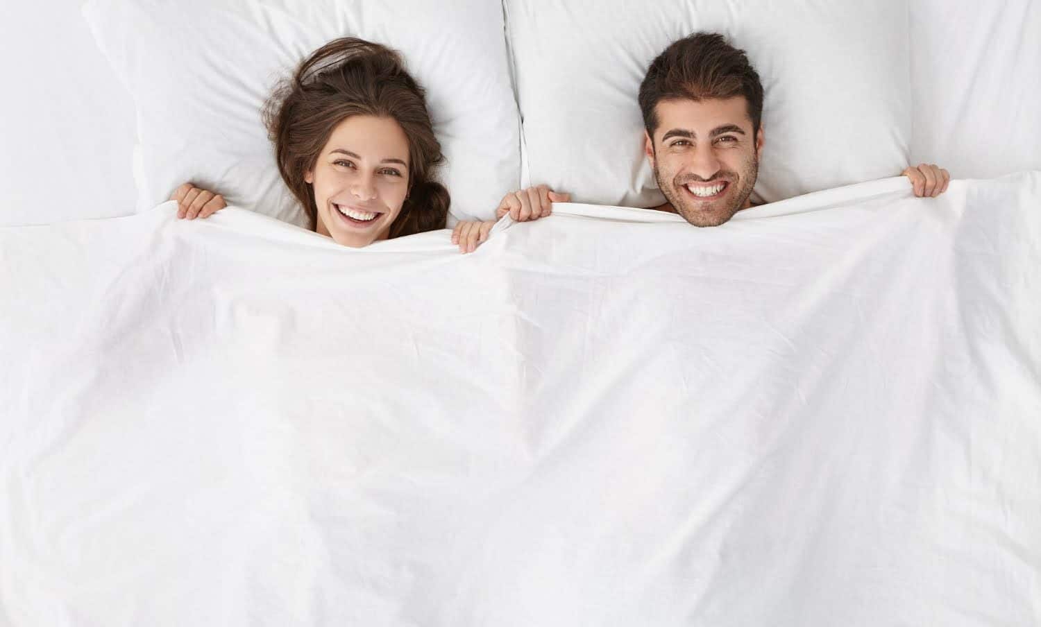 pareja acostada en la cama, tap&aacute;ndose con la s&aacute;bana hasta el cuelo, para dormir sin ropa