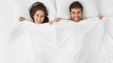 pareja acostada en la cama, tap&aacute;ndose con la s&aacute;bana hasta el cuelo, para dormir sin ropa