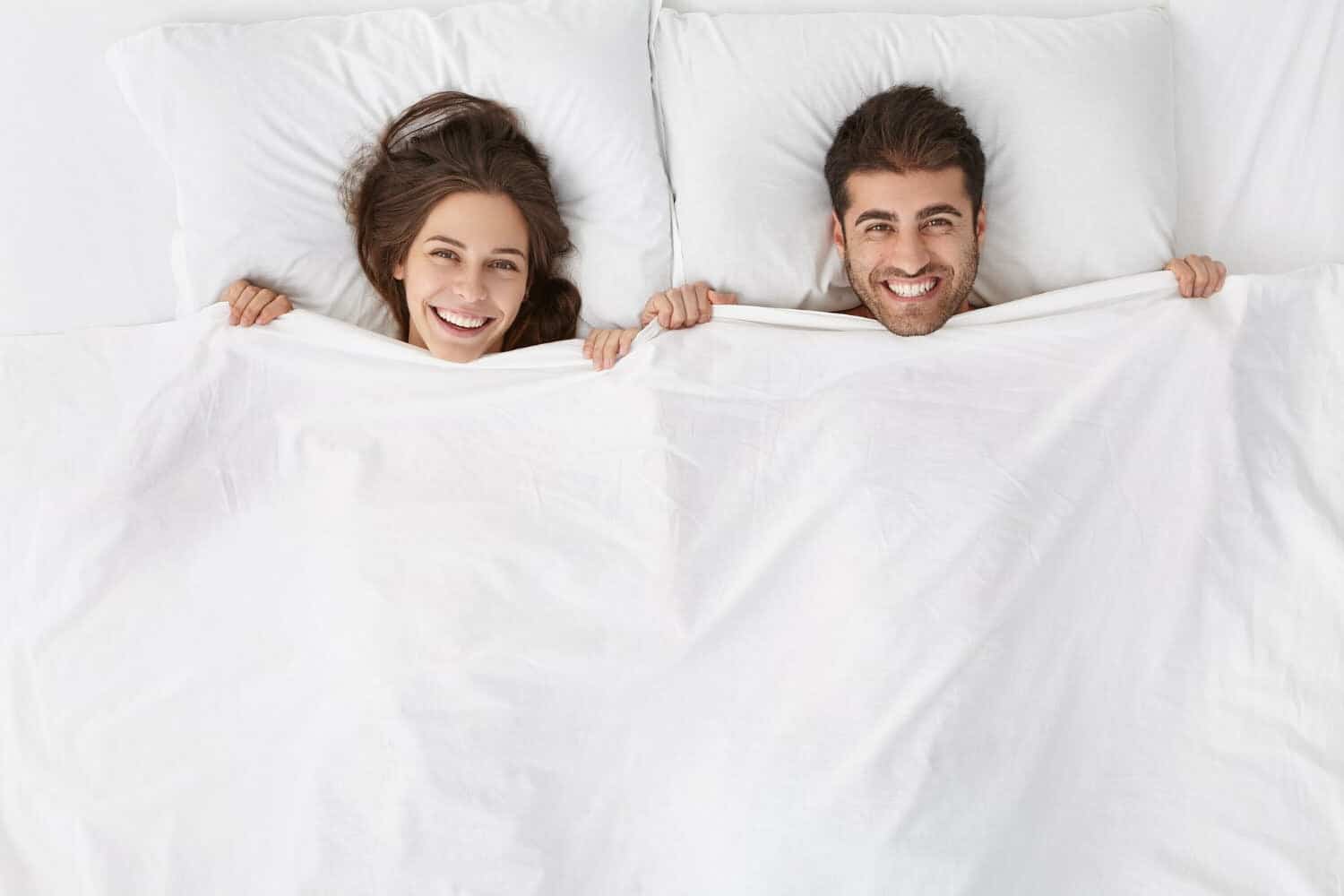 pareja acostada en la cama, tap&aacute;ndose con la s&aacute;bana hasta el cuelo, para dormir sin ropa
