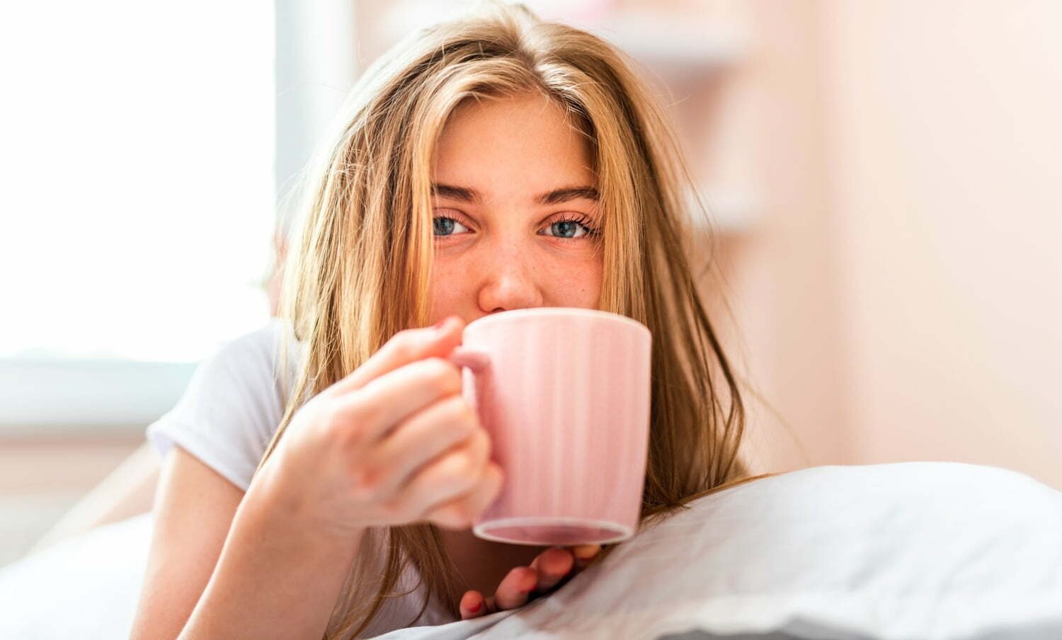 Mujer tomando café antes del desayuno, mientras está acostada en la cama
