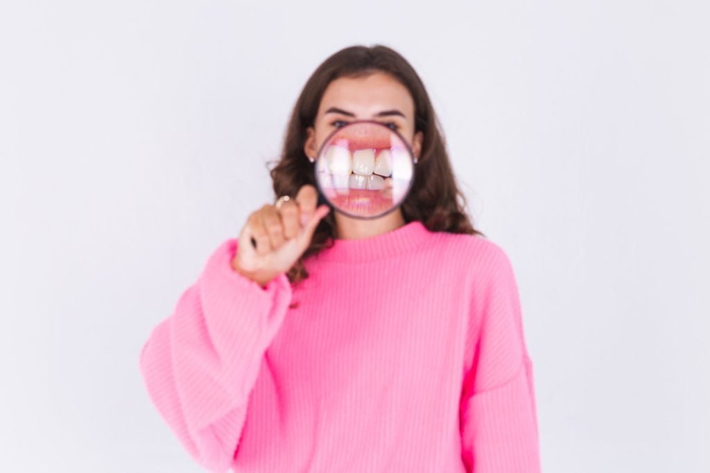 Mujer con una lupa sobre sus dientes, para ampliar la vista - gel reconstructor de dientes