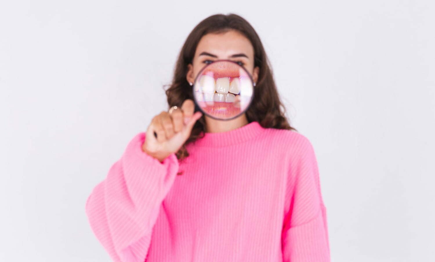 Mujer con una lupa sobre sus dientes, para ampliar la vista - gel reconstructor de dientes