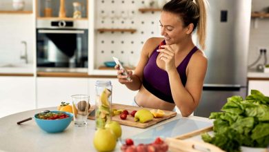 mujer con ropa de hacer ejercicio, comiendo frutas para perder peso, mientras mira su celular / Crisis de la mediana edad / masa muscular