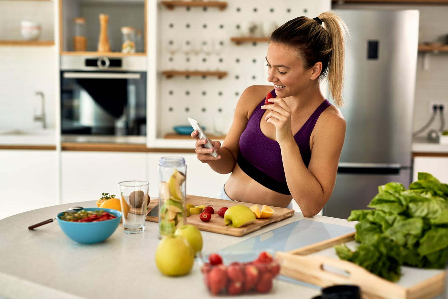 woman in exercise clothes, eating fruits to lose weight, while looking at her cell phone / Midlife crisis / muscle mass