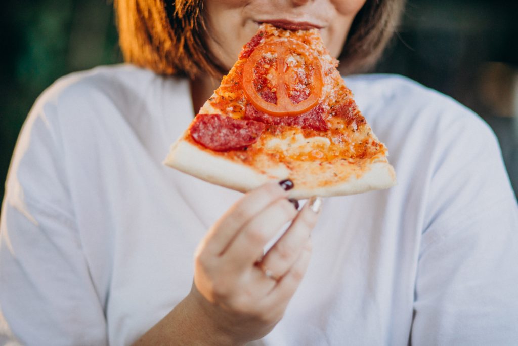 mujer joven que sufre de colesterol comiendo una porci&oacute;n de pizza