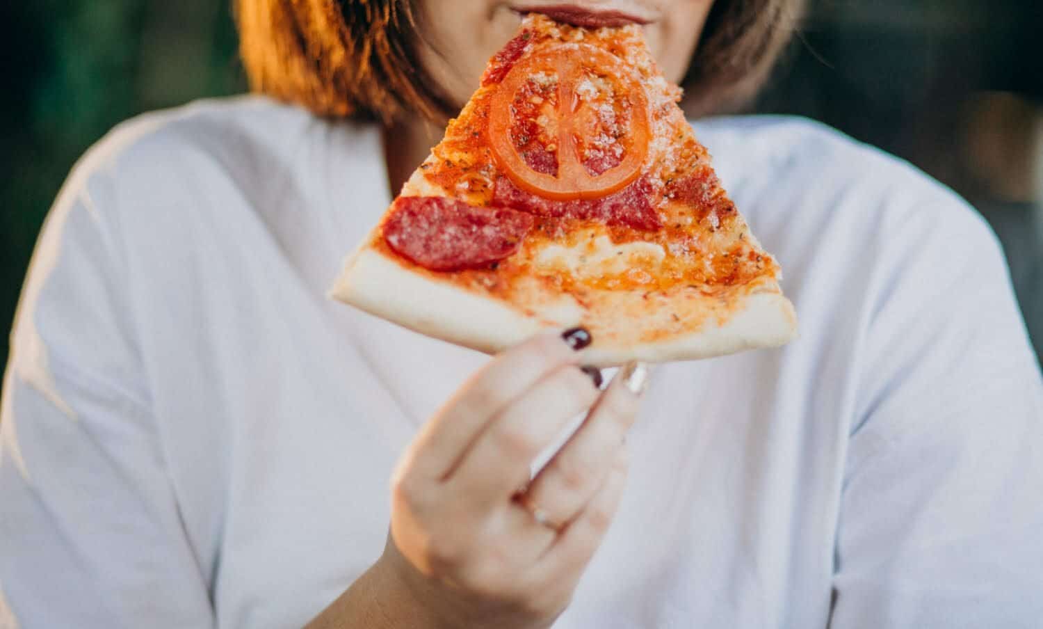 mujer joven que sufre de colesterol comiendo una porci&oacute;n de pizza
