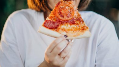 mujer joven que sufre de colesterol comiendo una porci&oacute;n de pizza