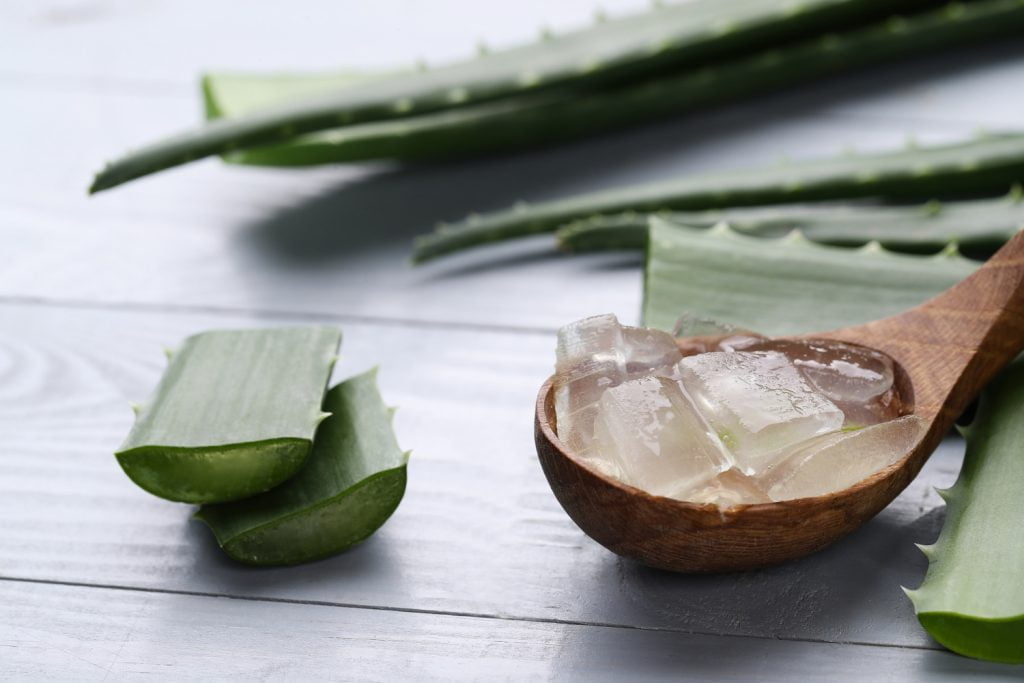 trozos de aloe vera para eliminar el acne, sobre cuchara de madera hojas de la planta.