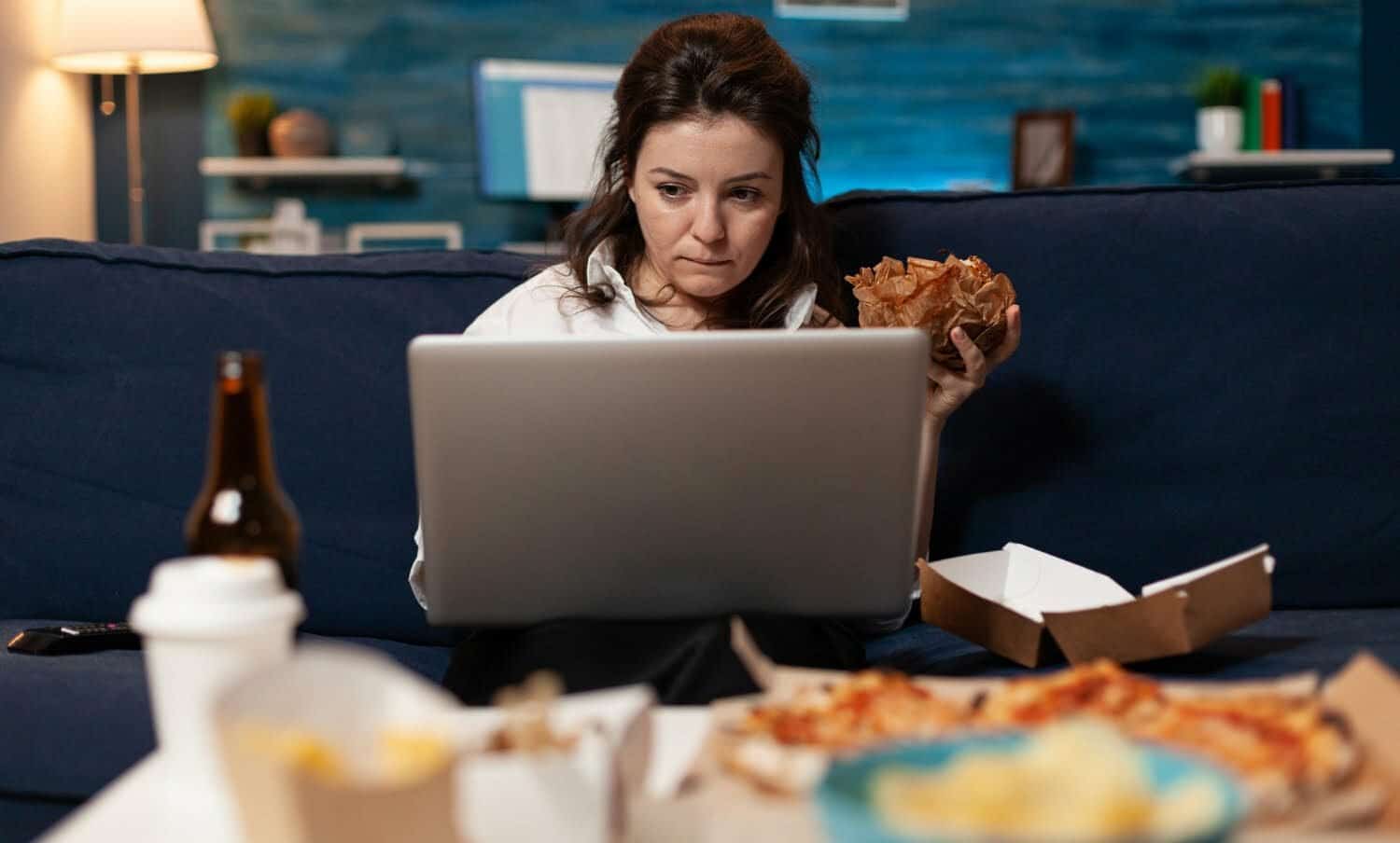 mujer sentada en el sof&aacute; comiendo una hamburguesa / estr&eacute;s