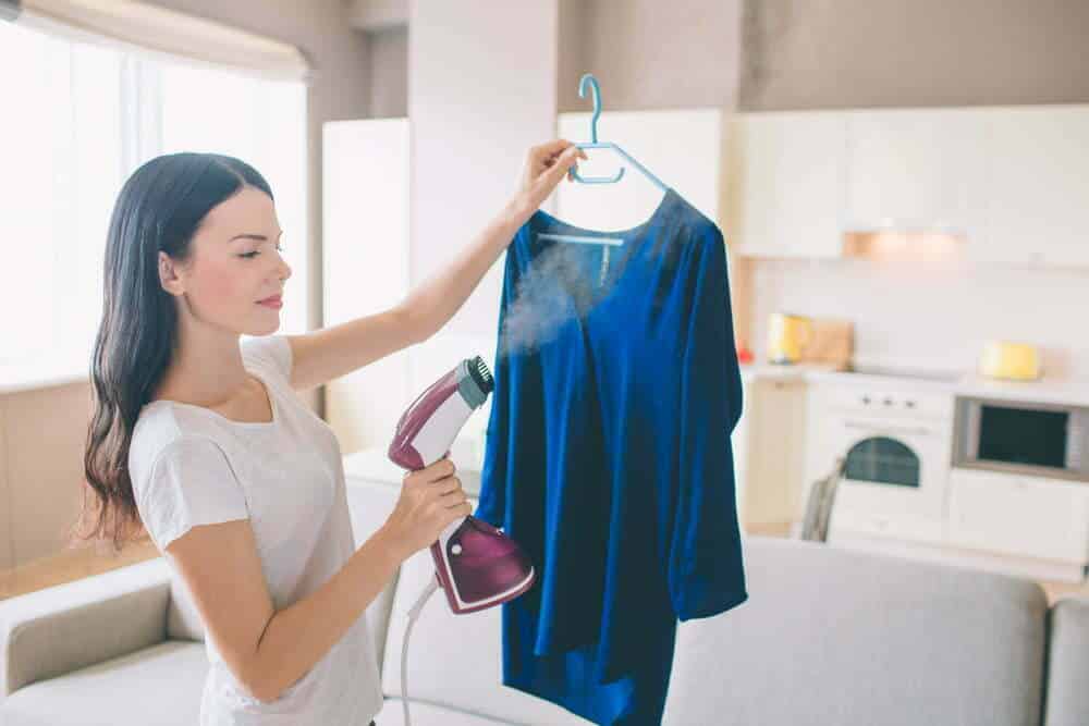 La mujer est&aacute; tomando una camisa azul en la habitaci&oacute;n / quitar las arrugas de la ropa / Secar la ropa