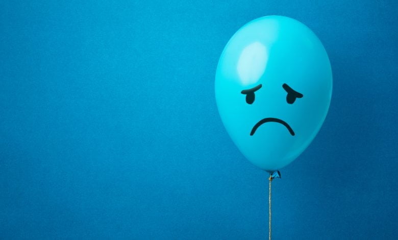 Foto de un globo azul sobre un fondo azul con una cara triste dibujada / blue monday