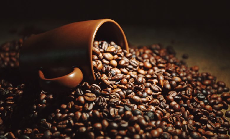 Una taza marrón y granos de café aromáticos esparcidos en un fondo de madera / cafeína