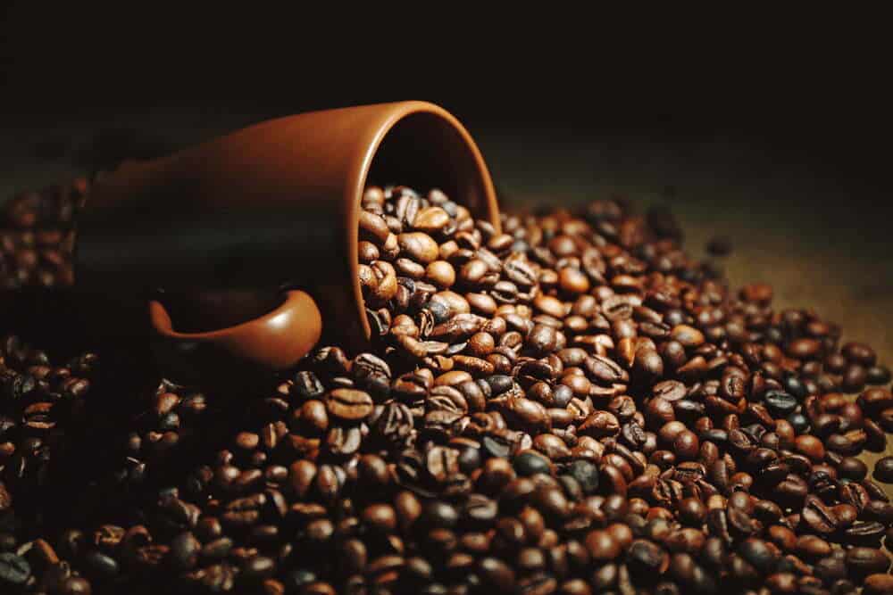 Una taza marr&oacute;n y granos de caf&eacute; arom&aacute;ticos esparcidos en un fondo de madera / cafe&iacute;na