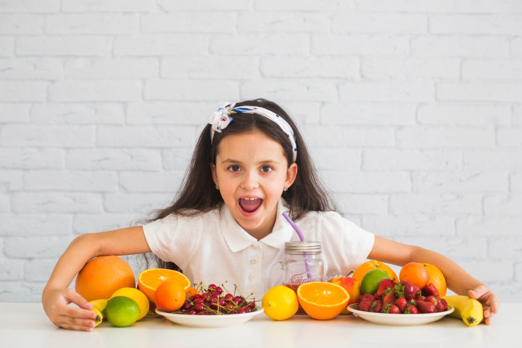 ni&ntilde;a con muchas frutas sobre una mesa