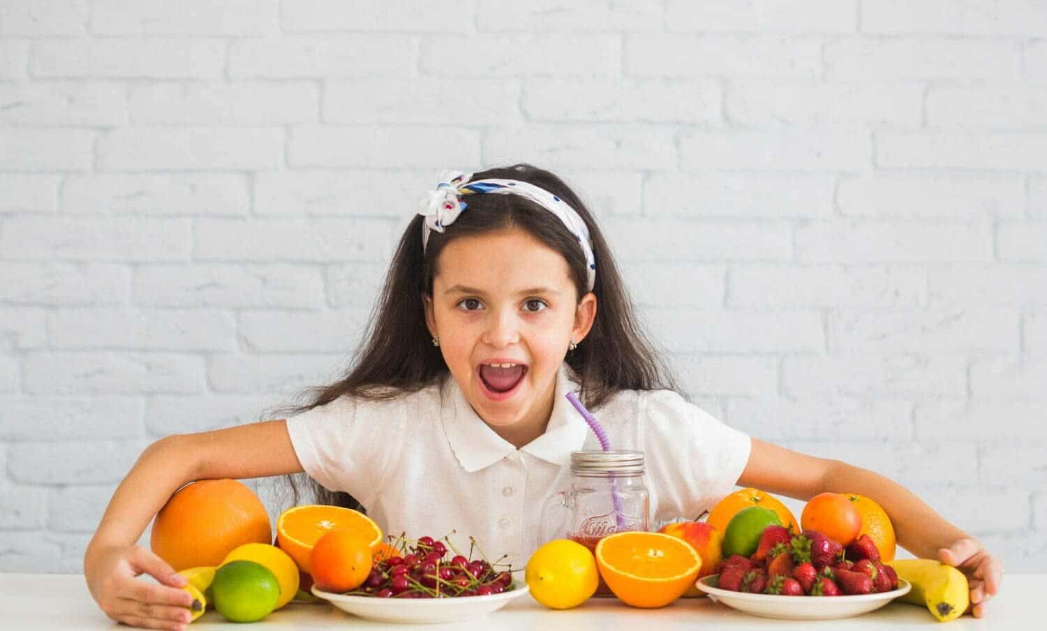 ni&ntilde;a con muchas frutas sobre una mesa
