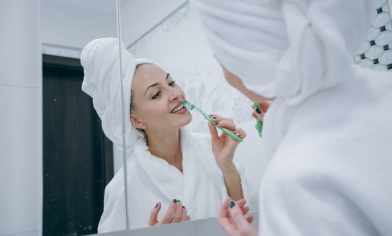 Mujer recién salida de la ducha, haciendo limpieza de sus dientes con un cepillo dental