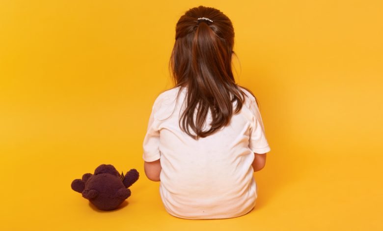 niña sentada de espalda, con osito de peluche marrón, víctima de maltrato infantil