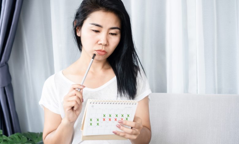 Mujer con problemas de amenorrea, periodos irregulares mirando el calendario / período menstrual / ciclo menstrual