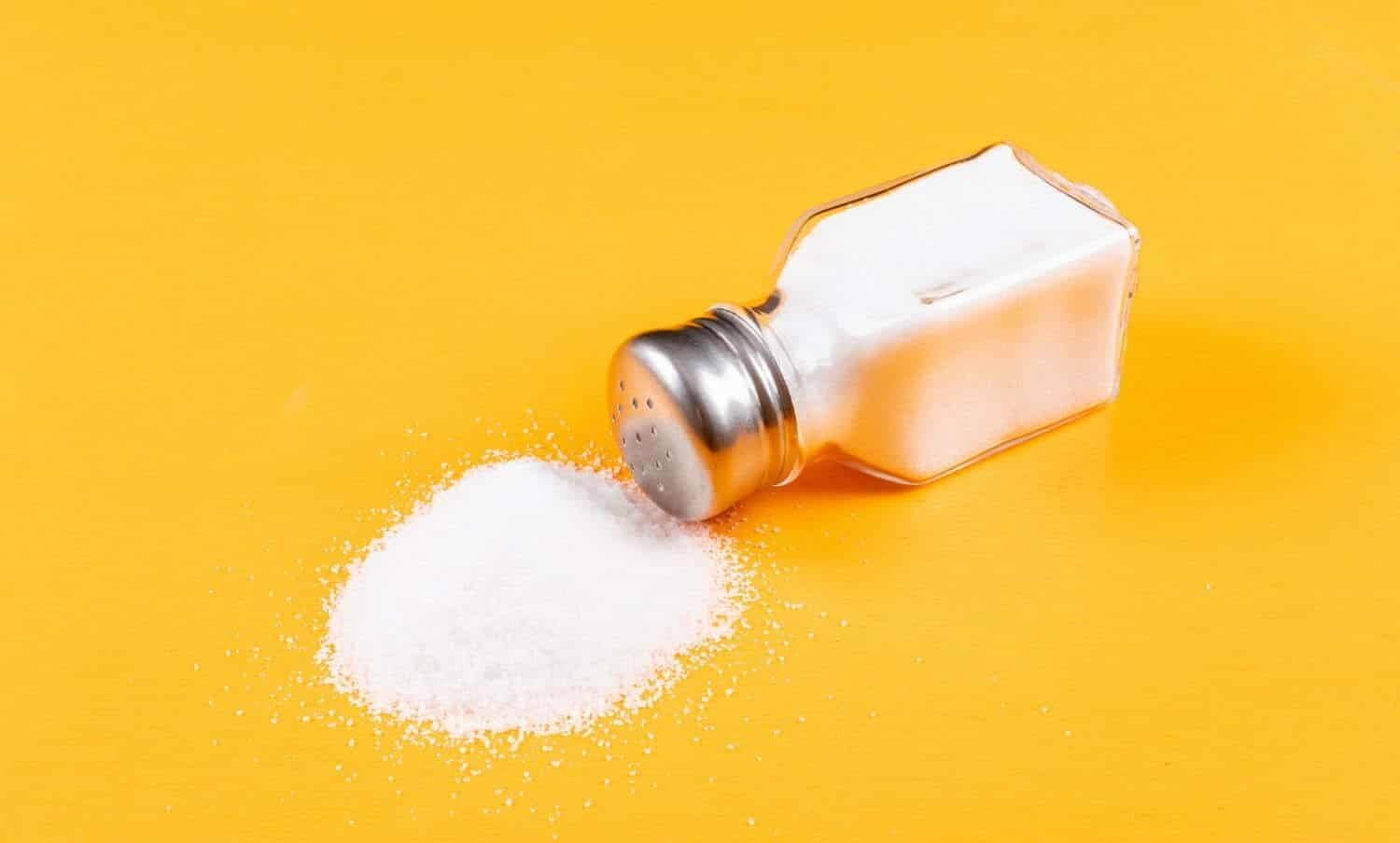 Salero derramando exceso de sal sobre fondo amarillo