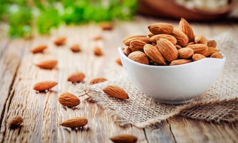 Almendras en taz&oacute;n blanco de porcelana sobre mesa de madera / snacks