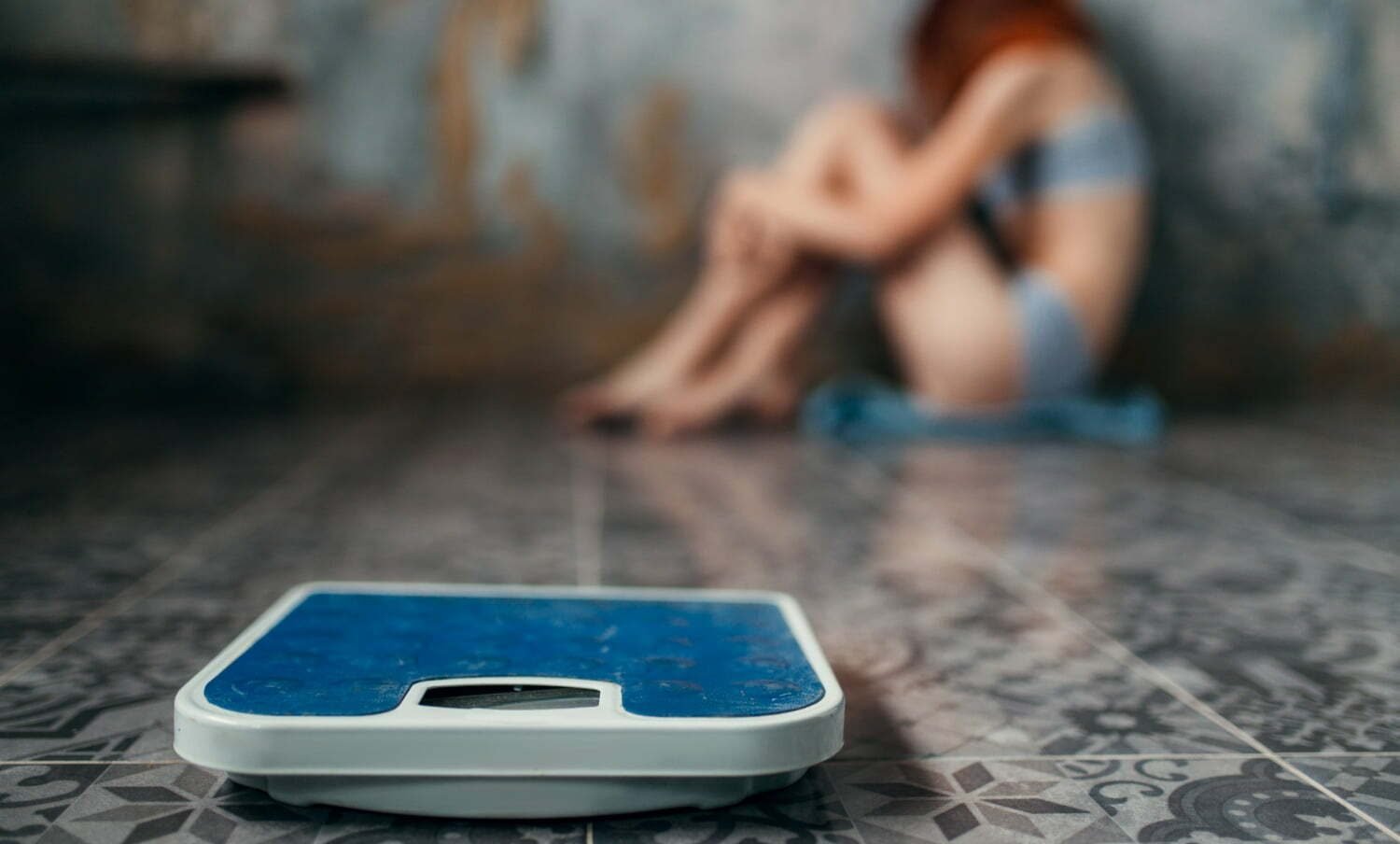 Mujer con anorexia nerviosa sentada en un rincón y un peso adelante / subir de peso