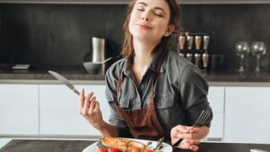 mujer muy joven sentada en la cocina comiendo pescado y tomates / menos calor&iacute;as