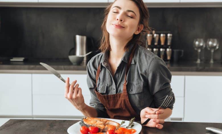 mujer muy joven sentada en la cocina comiendo pescado y tomates / menos calor&iacute;as