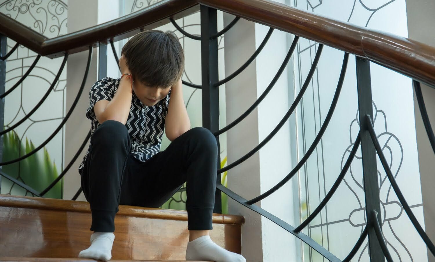 niño sentado en las escaleras de su casa, tapando sus oidos en un ataque de trastorno de ansiedad