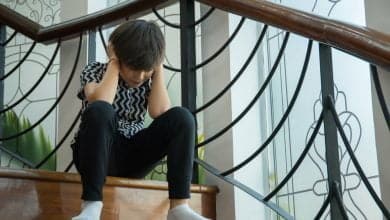 ni&ntilde;o sentado en las escaleras de su casa, tapando sus oidos en un ataque de trastorno de ansiedad / invalidaci&oacute;n emocional