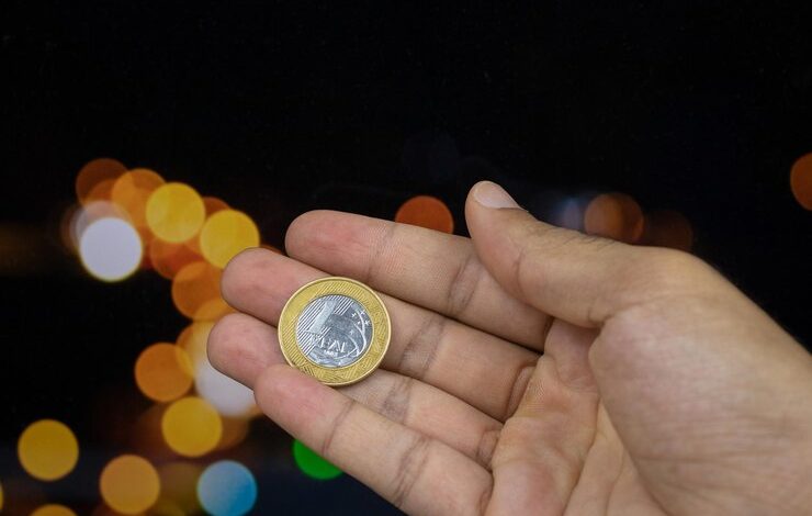 Foto sosteniendo una moneda de dinero brasile&ntilde;o en un fondo de luces borrosas