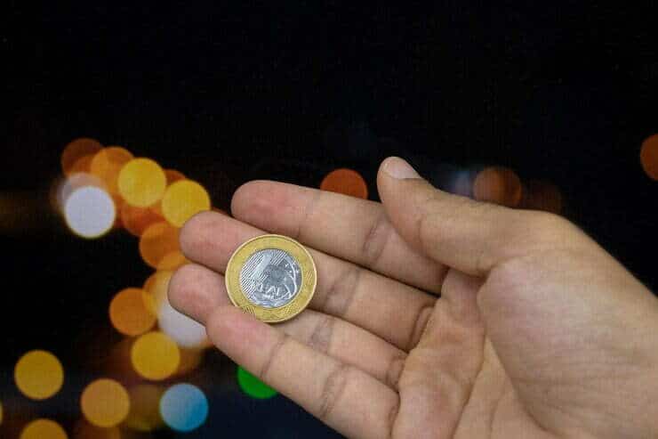Foto sosteniendo una moneda de dinero brasile&ntilde;o en un fondo de luces borrosas