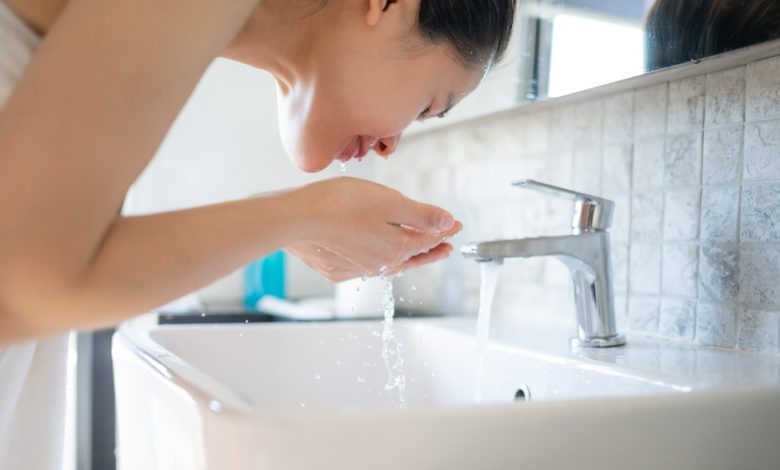 Mujer lavando su cara con agua fría en el lavabo del baño / agua helada